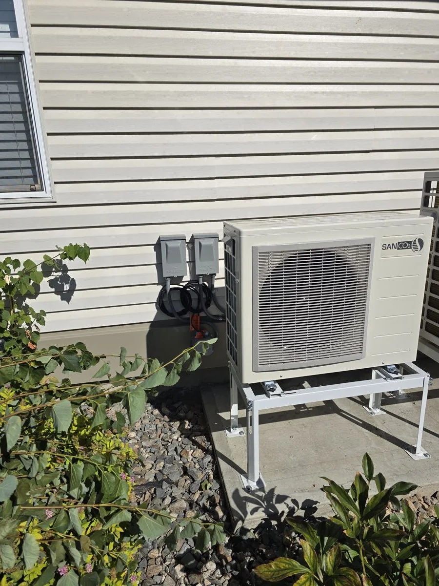 Outdoor heat pump condenser unit mounted on a wall bracket with electrical disconnects