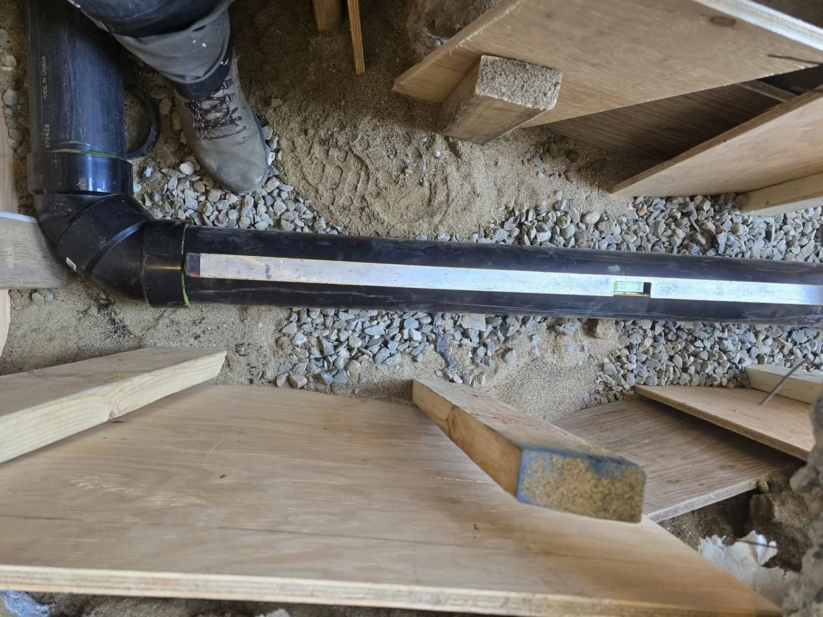 Underground drain run bedded in gravel beneath a floor system