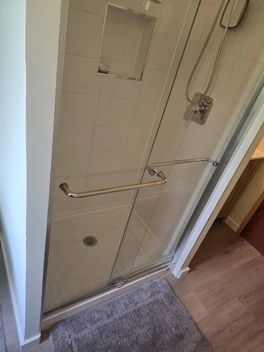 Glass shower enclosure with brushed hardware in a completed bathroom