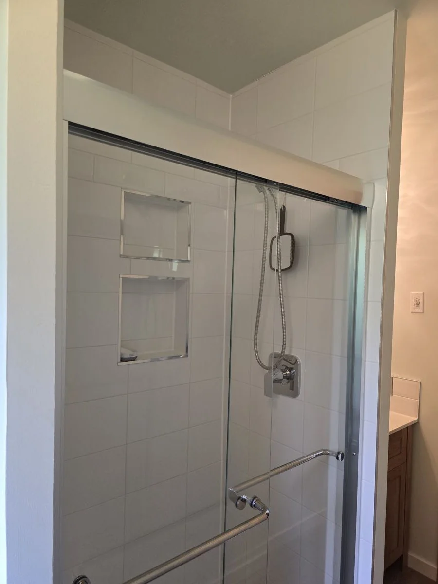 Tiled shower with sliding glass door and recessed shelving